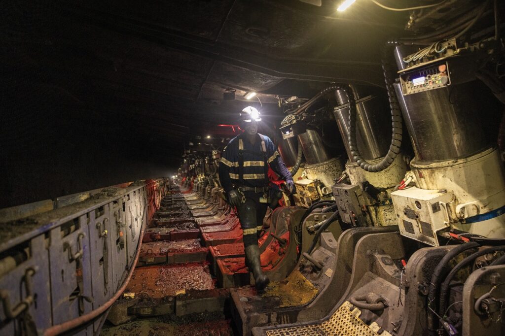 Workers in protective gear inspecting machinery in a dimly lit tunnel.