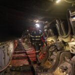 Workers in protective gear inspecting machinery in a dimly lit tunnel.